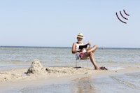 Moden mand sidder i en stol på stranden i direkte sollys uden solcreme på kroppen.